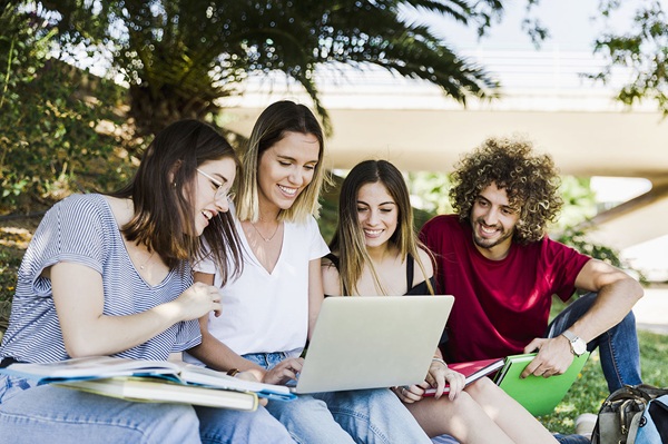 Personas que son estudiantes, sentados debajo de un árbol mirando un portátil